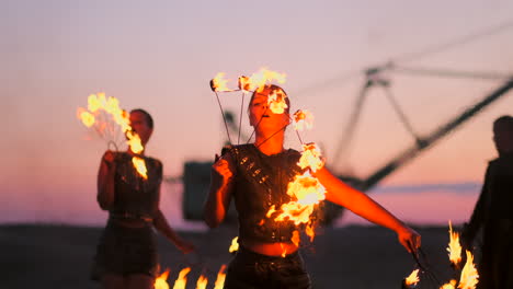 Mujeres-Con-Fuego-Al-Atardecer-En-La-Arena-Bailan-Y-Muestran-Trucos-Contra-El-Hermoso-Cielo-En-Cámara-Lenta